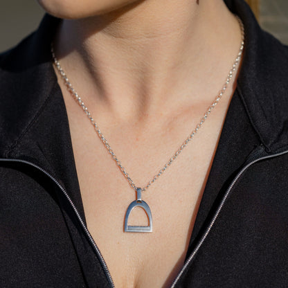 Equestrian person wearing a necklace with a horse stirrup pendant against a black background