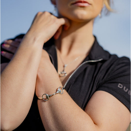 horse rider wearing a black shirt with visible branding, holding their arm wearing a horse bit snaffle bangle made by Crawford Hill Equestrian Jewellery.