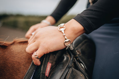 A horse rider riding a horse, wearing a three snaffle sterling silver bracelet and a sterling silver snaffle ring made by Crawford Hill Equestrian Jewellery. 
